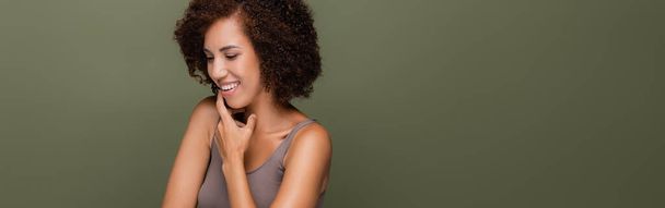 Pretty african american woman in top touching chin isolated on green, banner  - Foto, Imagem