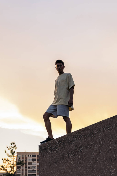 Magabiztos fiatalember alkalmi ruhát visel, pózol és kamerába néz gyönyörű naplemente ellen a városban.. - Fotó, kép