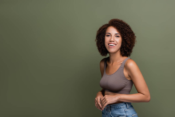Pretty african american woman in top and jeans looking at camera isolated on green  - Foto, imagen