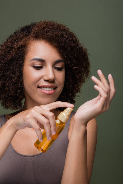 Femme afro-américaine positive appliquant de l'huile cosmétique à la main isolée sur vert  - Photo, image