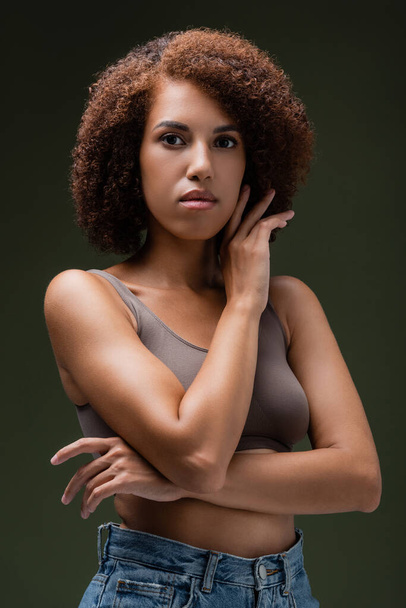 Portrait of curly african american woman in top posing and looking at camera isolated on dark green  - Foto, immagini