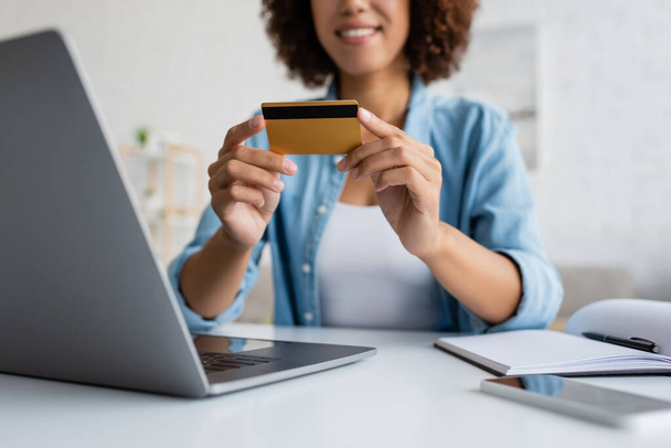 Cropped view of blurred african american woman holding credit card near devices  - Fotó, kép