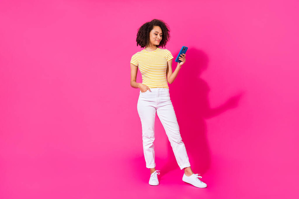 Full size foto van mooie jonge meisje houden apparaat type lees e-mail slijtage trendy geel gestreept kledingstuk geïsoleerd op fel roze kleur achtergrond. - Foto, afbeelding