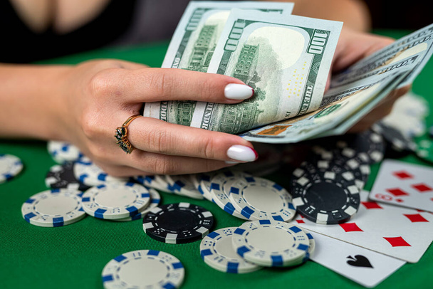 όμορφη γυναίκα παίκτης μετράει μάρκες για τα χρήματα και αυξάνει κατά τη διάρκεια του παιχνιδιού πόκερ στο καζίνο. ιδέα τζόγου. Μια γυναίκα με φόρεμα σε καζίνο. δολάρια και μάρκες - Φωτογραφία, εικόνα