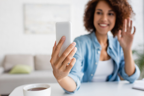 Blurred african american woman having video call on smartphone near cup of tea at home  - Fotografie, Obrázek