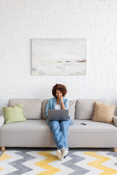 cheerful african american woman using laptop while sitting on couch and working from home  - Φωτογραφία, εικόνα