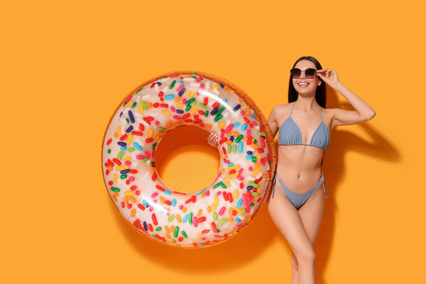 Young woman with stylish sunglasses holding inflatable ring against orange background - 写真・画像