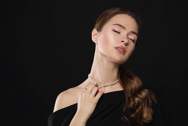 Young woman wearing elegant pearl jewelry on black background, space for text - Фото, зображення