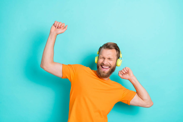 Photo of ecstatic funny man with blond hairstyle dressed orange t-shirt eyes closed raise fists up isolated on teal color background. - 写真・画像