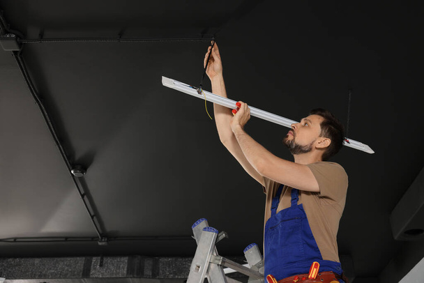 Electrician in uniform installing ceiling lamp indoors, low angle view - Foto, Imagem
