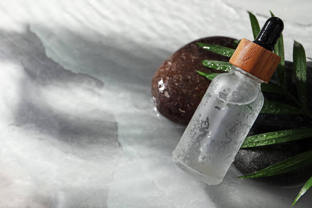 Bottle of face serum, spa stones and leaf on wet grey marble table, closeup. Space for text - Фото, изображение