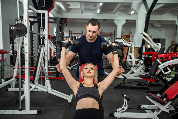 Fit weibliche Klientin beim Training mit persönlichem männlichen Trainer mit schweren Hanteln im Fitnessstudio. Sport für einen gesunden Lebensstil - Foto, Bild