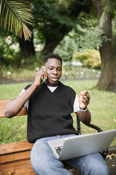 Young African man talking on phone disputing over computer, stressed, unsatisfied. Disappointed, confused, angry male arguing with technical online support or customer service. Bad connection concept - Foto, Imagem