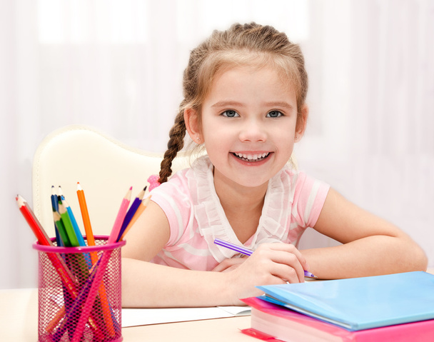 Cute smiling little girl is writing at the desk - Photo, Image