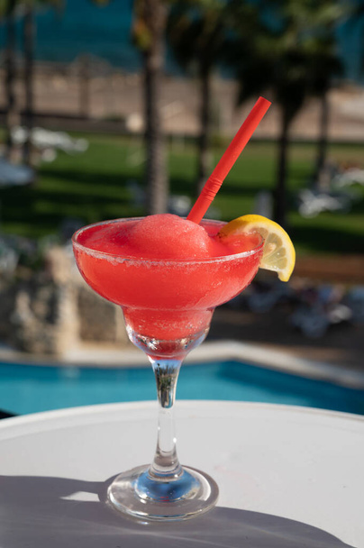 Colorido helado rosa fresa daiquiri cóctel servido en vidrio en la cafetería al aire libre con vistas a la piscina azul, el mar y las palmeras, relajarse y vacaciones en el mar - Foto, Imagen