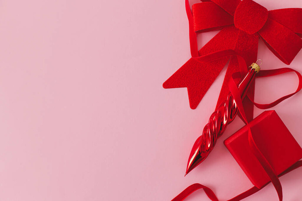 Современная рождественская розовая квартира лежала. Стильный красный бант, бамбук, подарок и лента на розовом фоне. Креативный минимальный фон с пространством для текста. Счастливого Рождества и счастливых праздников! - Фото, изображение