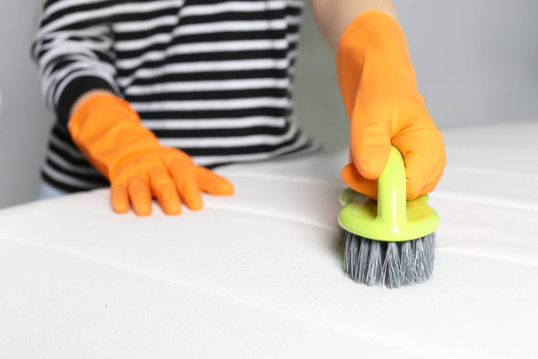 Woman in orange gloves cleaning white mattress with brush indoors, closeup - Photo, Image