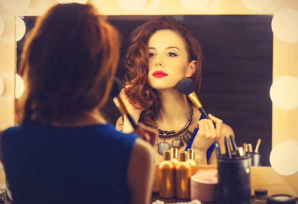 Portrait of a beautiful woman as applying makeup near a mirror - Photo, Image