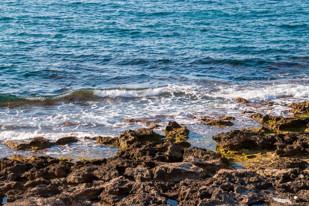 Fala pęka na skalistym wybrzeżu miasta Monopoli, Puglia, Włochy. Głęboki błękitny Adriatyk w słoneczny letni dzień. - Zdjęcie, obraz