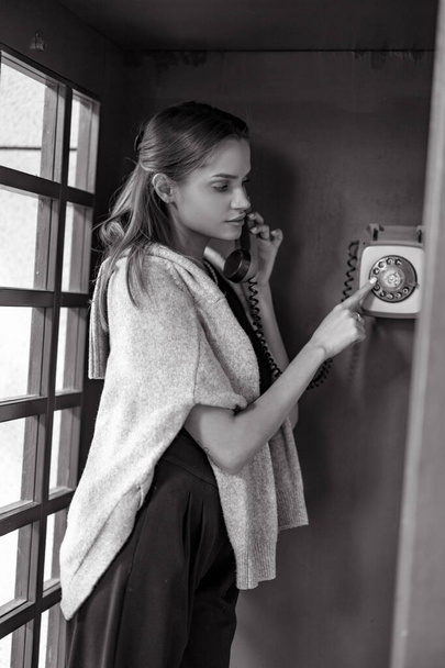 Young woman dials phone number in payphone booth. Closeup. Black and white image. - Fotoğraf, Görsel