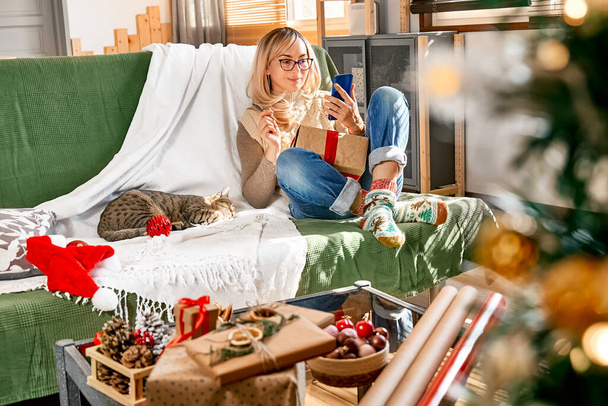 Vánoční prázdniny online nakupování doma. Happy blond žena nákup dárky pomocí smartphone pro vyhledávání propagaci na Černý pátek nebo kybernetické pondělí. - Fotografie, Obrázek