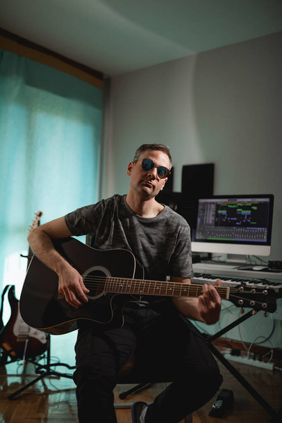 Music producer strumming some chords with the acoustic guitar while recording a new project at his home studio - 写真・画像