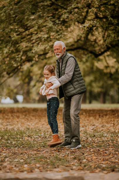 Knappe grootvader brengt tijd door met zijn kleindochter in het park op herfstdag - Foto, afbeelding