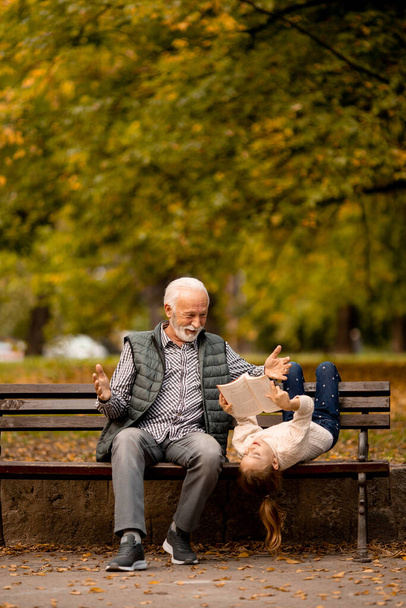 Όμορφος παππούς περνάει χρόνο με την εγγονή του στο παγκάκι την ημέρα του φθινοπώρου. - Φωτογραφία, εικόνα
