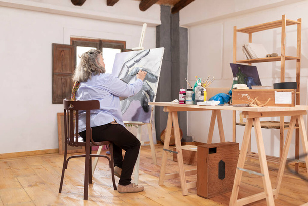 Зрелая женщина проводит досуг, развивая свои навыки рисования в мастерской. - Фото, изображение
