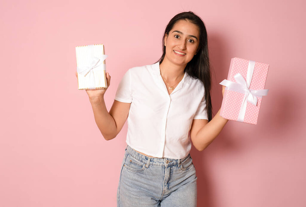 Portrait of an excited hispanic happy girl holding a gift box present on her head and looking at camera isolated over pink background - Valokuva, kuva