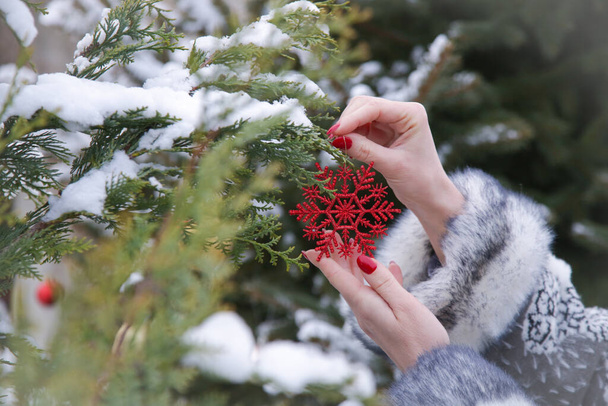 Vrouw versieren outdoor kerstboom met rode kerst sneeuwvlok ornament. Vakantie en winter concept. - Foto, afbeelding