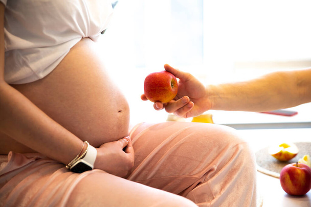 Man holding apple near pregnant woman. Healthy food during pregnancy. Vitamins and fruit. - Photo, image