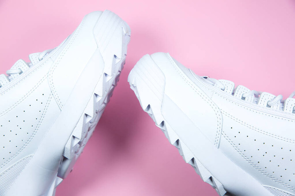 Μοντέρνα αθλητικά παπούτσια σε ροζ φόντο. Άσπρα δερμάτινα αθλητικά παπούτσια σε μεγάλη σόλα με καρφιά. Κλείσε.. - Φωτογραφία, εικόνα