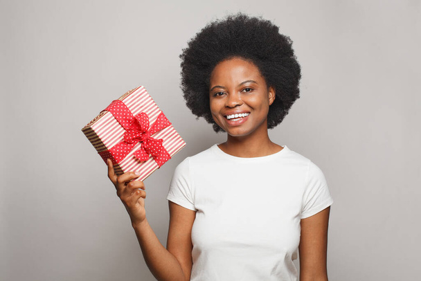 Beautiful smiling woman wearing white t-shirt showing red gift box against white studio wall banner background - Valokuva, kuva