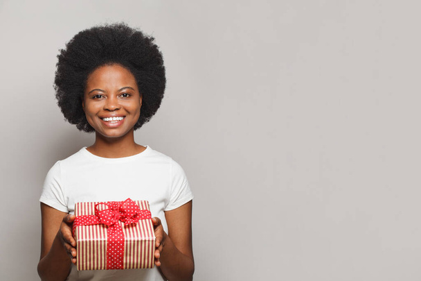 Πολύ φιλική θετική χαμογελαστή γυναίκα με κόκκινο κουτί δώρου κοιτάζοντας κάμερα σε λευκό φόντο - Φωτογραφία, εικόνα