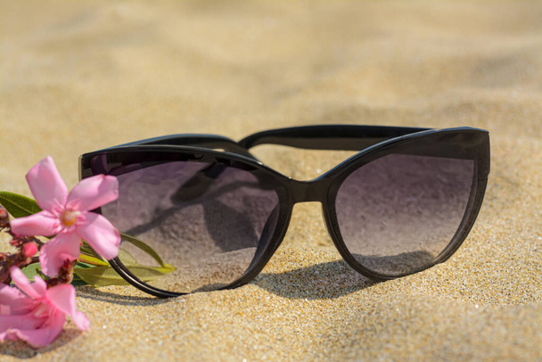 Beautiful sunglasses with flower on sand, closeup - Photo, Image