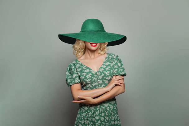 Femme heureuse avec des cheveux bouclés blonds portant une robe verte et un chapeau vert large et souriant - Photo, image