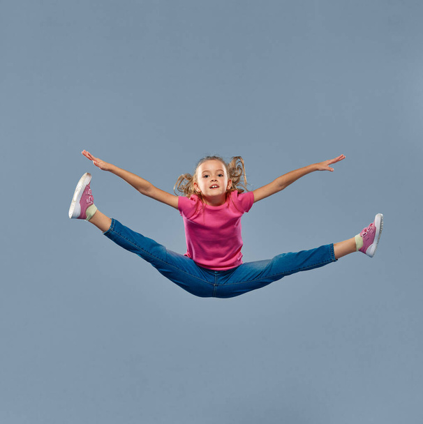 Portrait of little beautiful girl, child in casual clothing posing, jumping in a twine isolated over grey studio background. Concept of childhood, emotions, facial expression, active lifestyle - Fotoğraf, Görsel