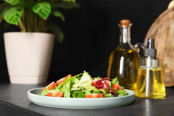 Plate of salad and bottles with cooking oil on black table in kitchen - Photo, Image