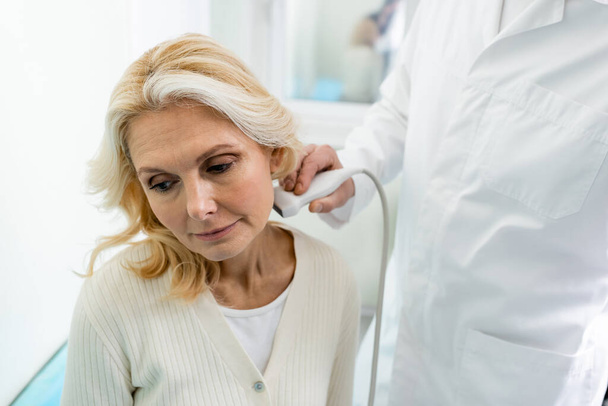 医師は中年女性の首にリンパ節の超音波検査を行い - 写真・画像
