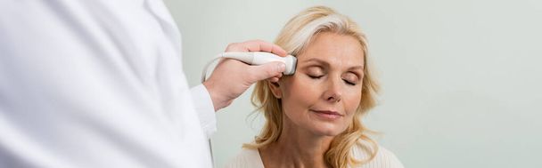 blond vrouw met gesloten ogen in de buurt wazig arts doen echografie van haar hoofd, banner - Foto, afbeelding