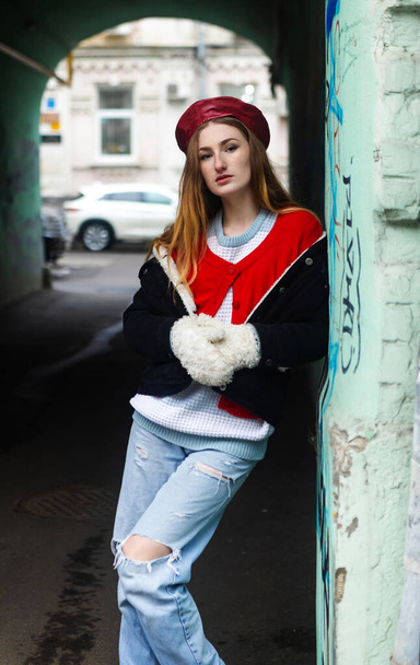 Francuski styl odzieży, uliczna moda. Piękna dziewczyna w płaszczu, czerwonym berecie i dżinsach spaceruje po starym mieście.. - Zdjęcie, obraz