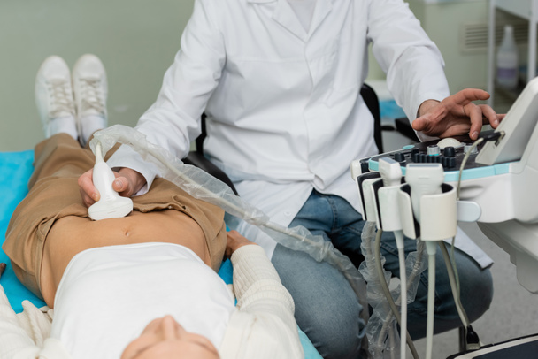 白衣を着た医師が横になっている女性の腎臓超音波検査を行い - 写真・画像