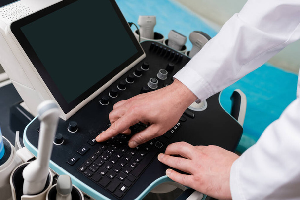 Boş ekranlı ultrason makinesinin kontrol panelini kullanan hekimin kırpılmış görüntüsü - Fotoğraf, Görsel