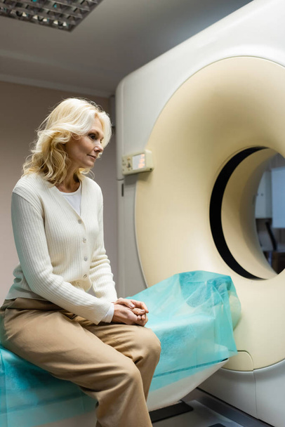 pensive middle aged woman sitting near ct scanner in hospital - Foto, immagini
