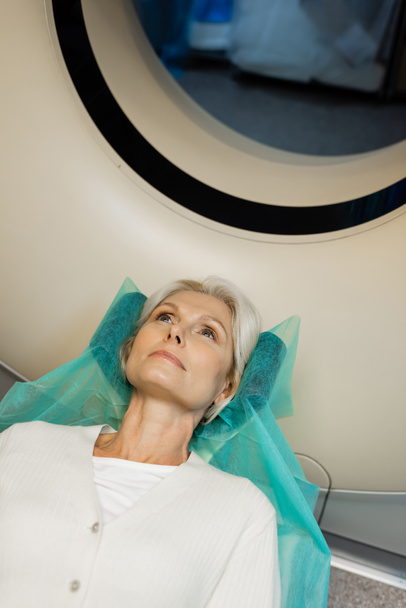 high angle view of blonde woman lying during diagnostics on ct scanner in hospital - Фото, изображение