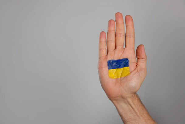 Man with drawing of Ukrainian flag on palm against light grey background, closeup. Space for text - Zdjęcie, obraz