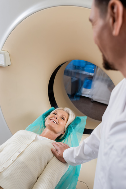 wazig radioloog kalmerende lachende vrouw tijdens computertomografie in kliniek - Foto, afbeelding