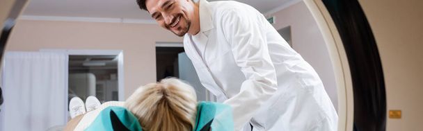 radiólogo de capa blanca sonriendo cerca de la mujer y la máquina de tomografía computarizada, pancarta - Foto, Imagen