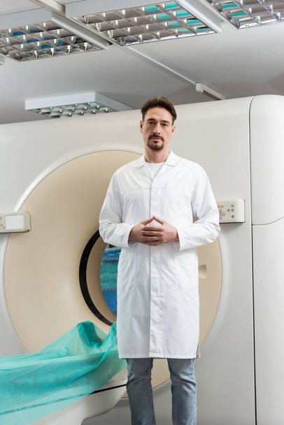 serious bearded radiologist looking at camera near computed tomography scanner in clinic - 写真・画像